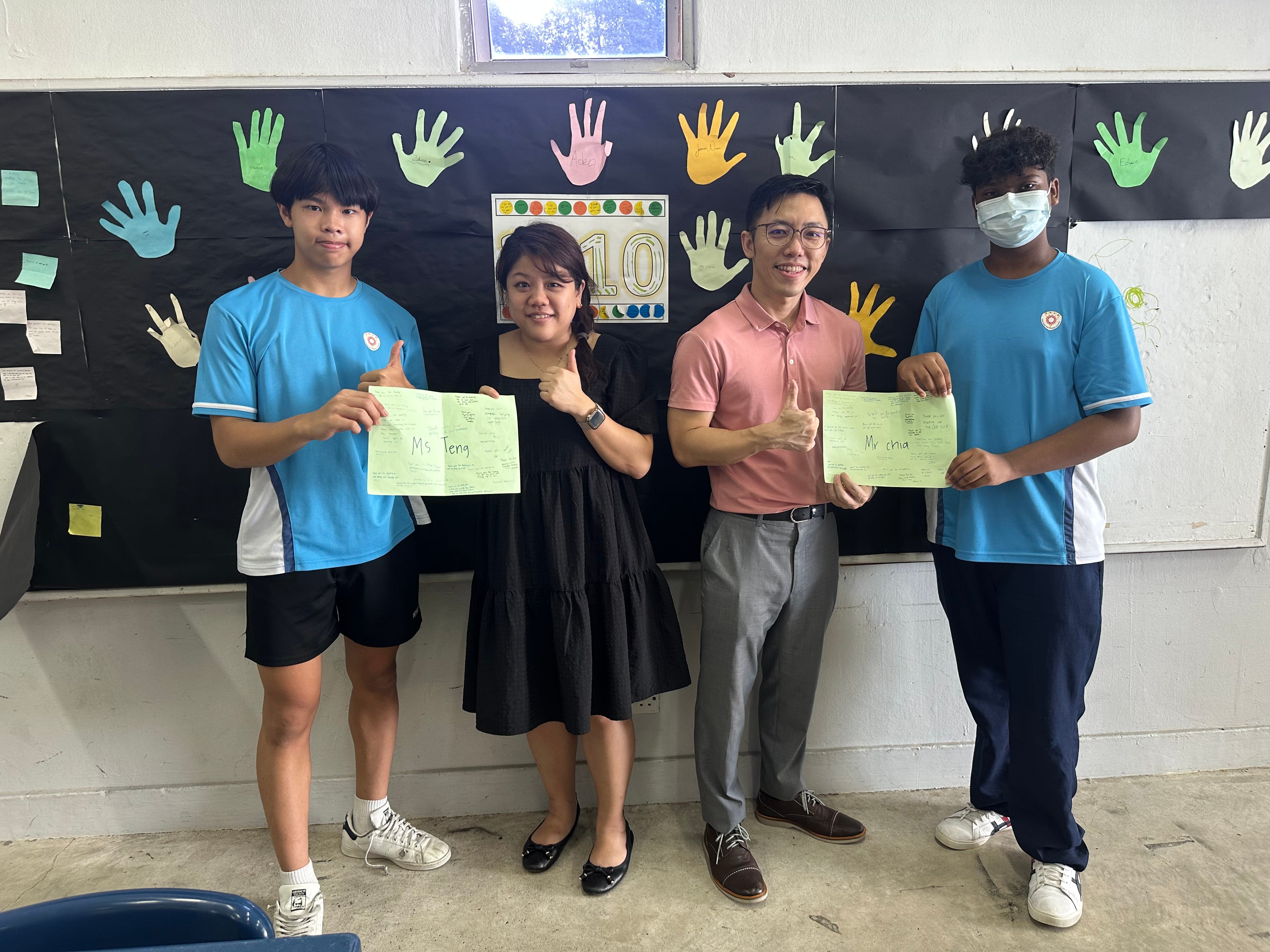 A group of students pictured holding sheets of paper with heartfelt messages on them, presenting it to their form teacher